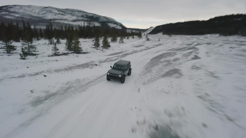 Truck traveling through the snow covered terrain between forests and mountains