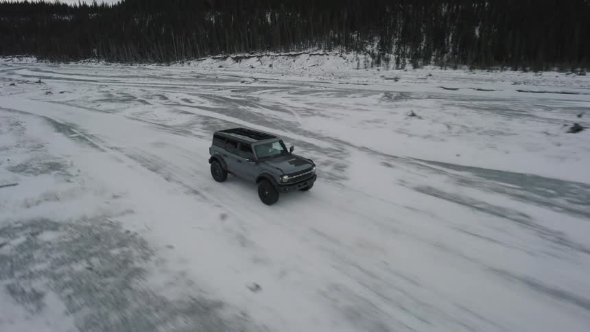 Gray suv driving on a snowcovered road with forest in the background