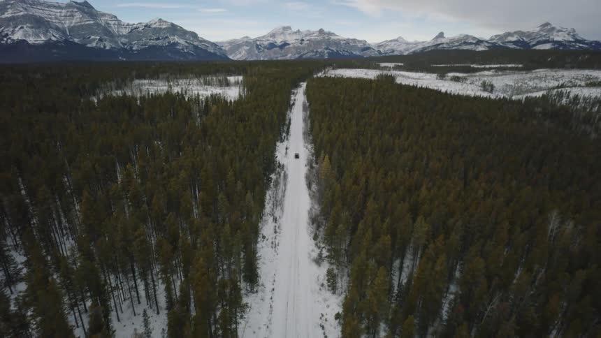 Automobile traveling on a snow covered road through a forest with mountains in the distance