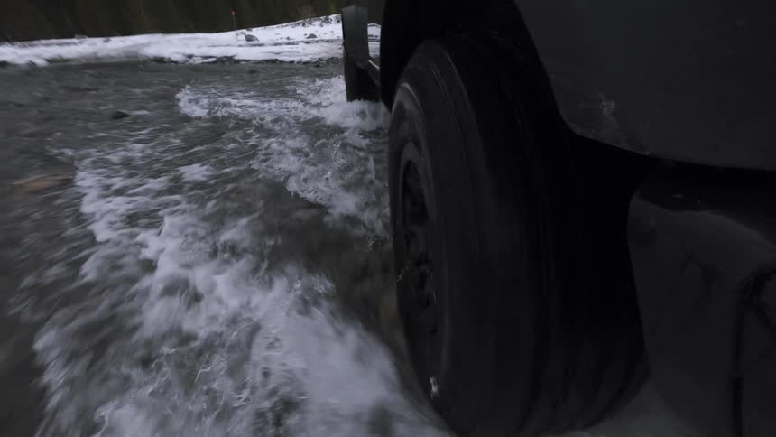 Truck wheel moves through pooled water on a road with snow along the sides