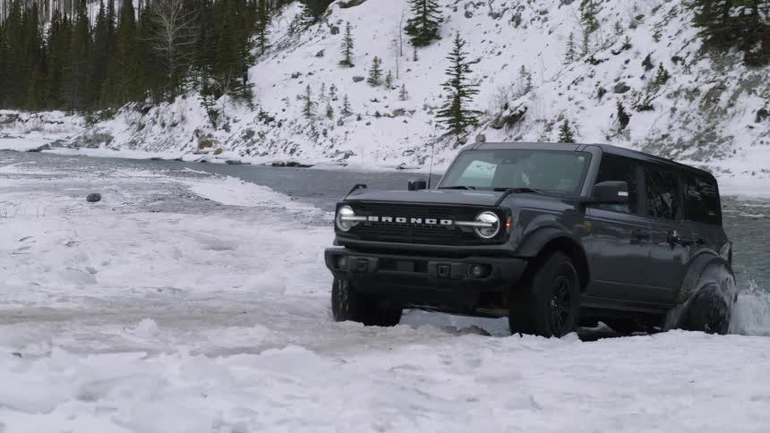 A bronco suv driving away from a lake into a snowfilled landscape during winter at midday