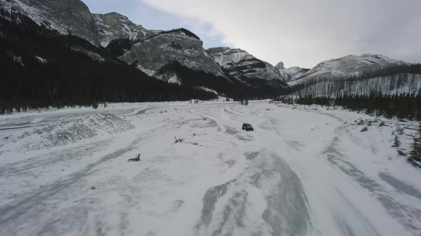A black suv drives on a snowy road through a vast mountain valley