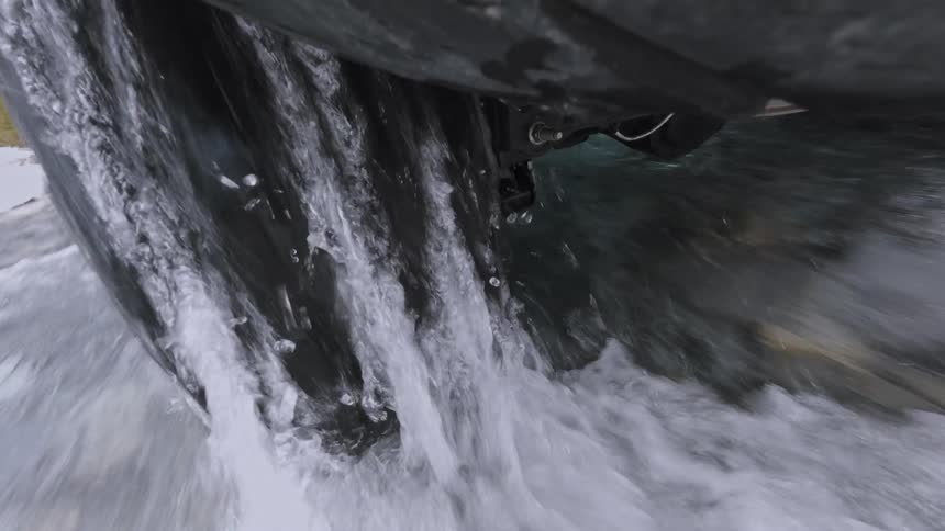 Vehicle wheel moves through flowing water creating splashes