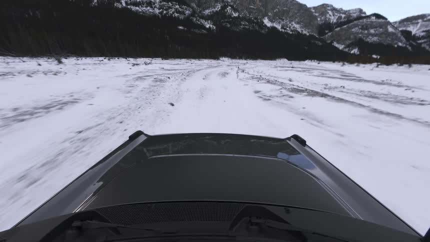 Vehicle hood moving along a snowcovered trail with mountains in the background