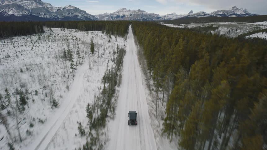 Vehicle driving along a snowcovered road between forest and mountains