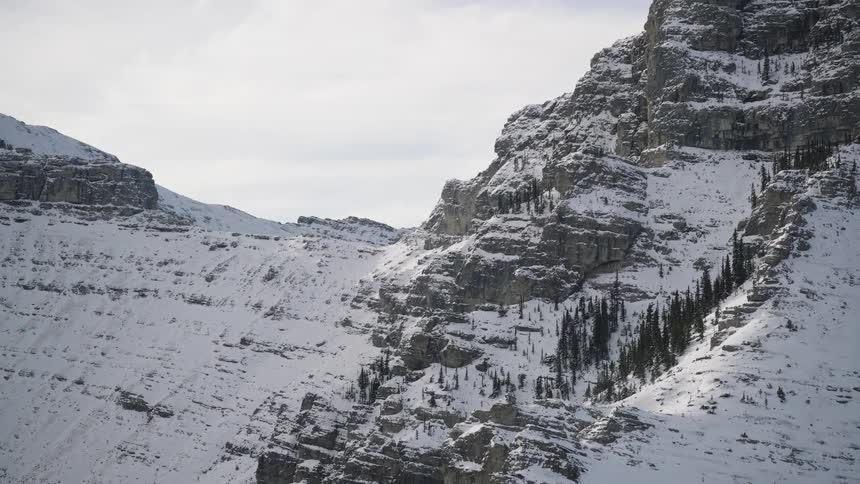 Snow covers the rough terrain of mountains under a cloudy winter sky