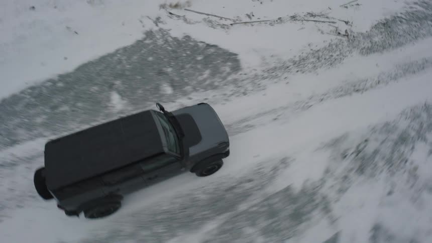 Suv driving across a wide snowcovered area with tracks marked on the ground