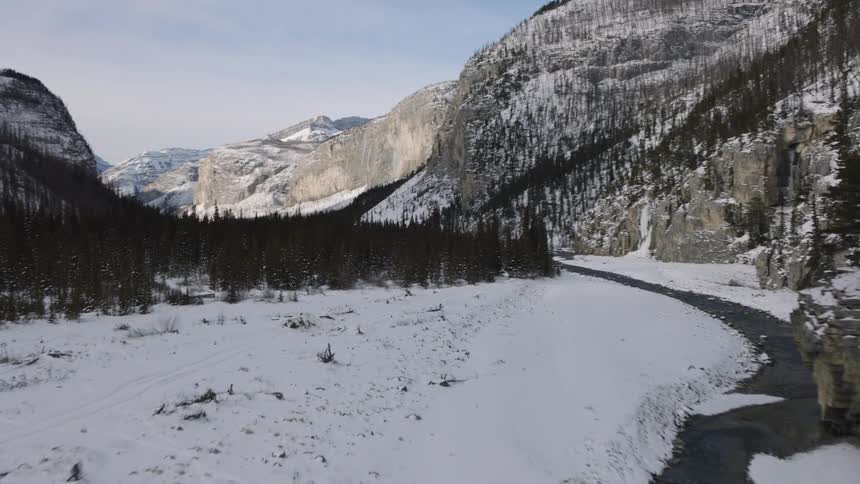 Stream running through a snow covered forested mountain valley with mountains in the distance