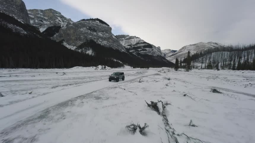 Truck traveling through the snow covered terrain in the valley between forests and mountains
