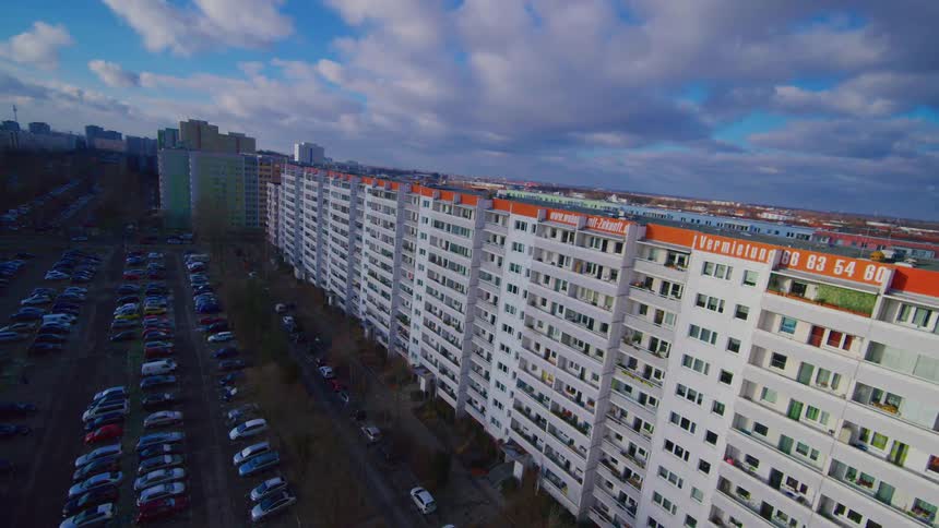 Row of residential apartment buildings beside a parking lot filled with cars under a partly cloudy sky