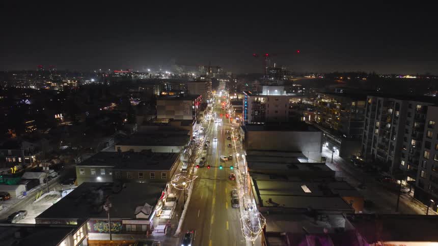 Vehicles drive along a street passing residential buildings on a winter night