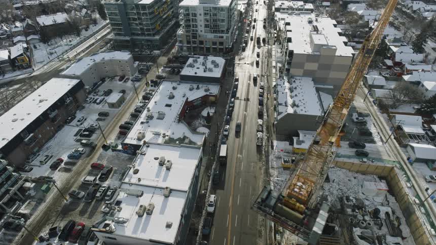 Traffic moves on city streets between buildings and cars in parking lots