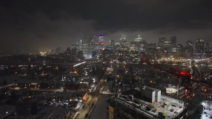 Nighttime city skyline with illuminated skyscrapers and a crane beside a building under construction