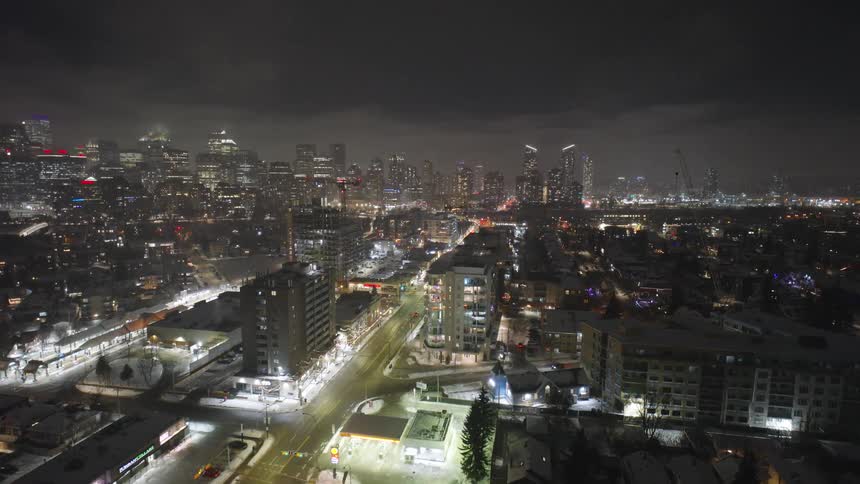 Aerial nighttime view of an illuminated avenue with buildings and surrounding neighborhoods