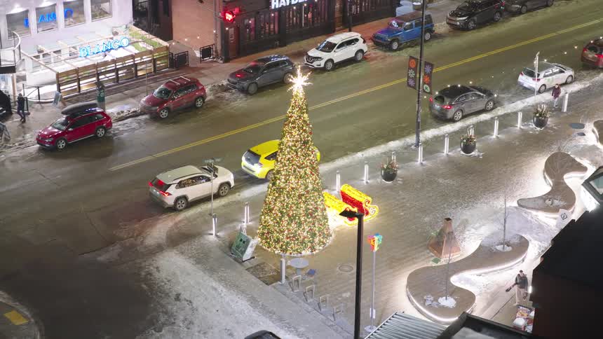 Cars park on the streets in front of stores as a pedestrian walks by a christmas display