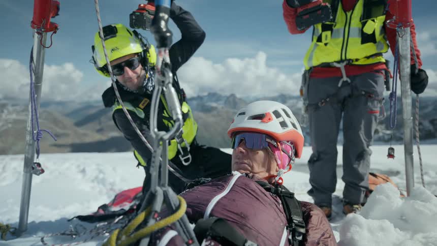 Two mountain rescue workers lift an injured hiker with a cable