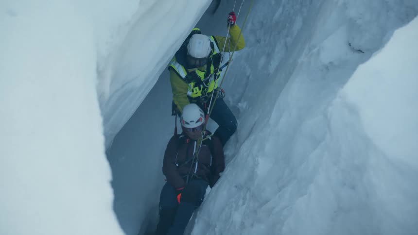 One ice climber helps to lift another from an icy crevasse