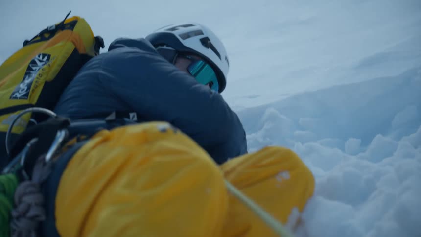 A mountaineer navigating a steep snowcovered slope in a harsh winter environmentthe climber outfitted in professional highaltitude gear and bright yellow trousers carefully uses an ice axe for stability as they ascend through deep powdery snow