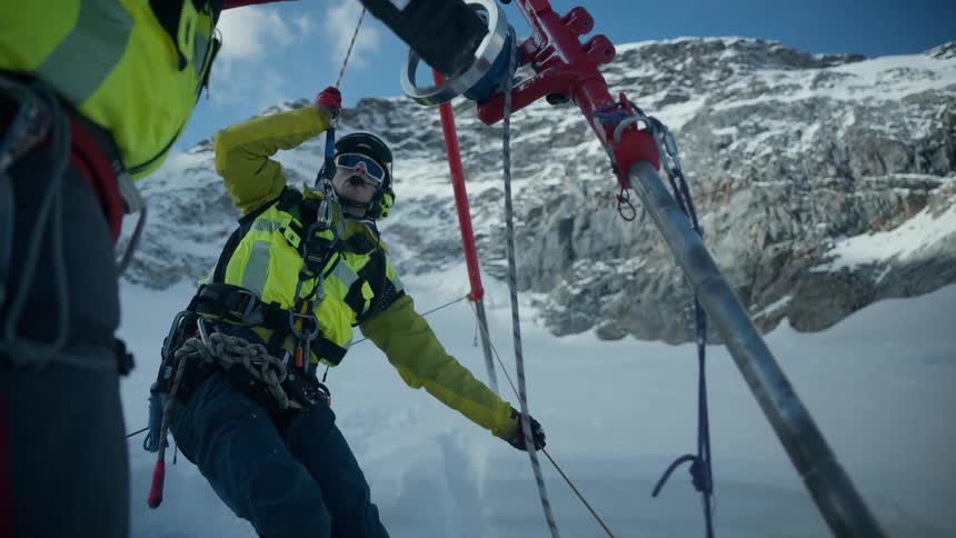Professional with safety equipment working suspended on a metal structure over a snowy area