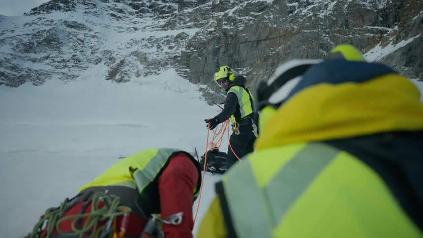 Mountain climbers connected by ropes move across a snowy slope on a winter day