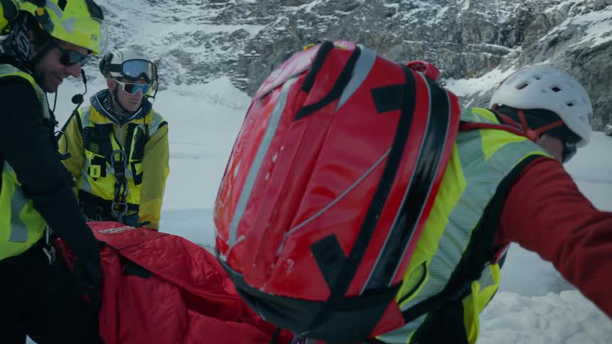A group of rescuers carry a person across a snow covered landscape