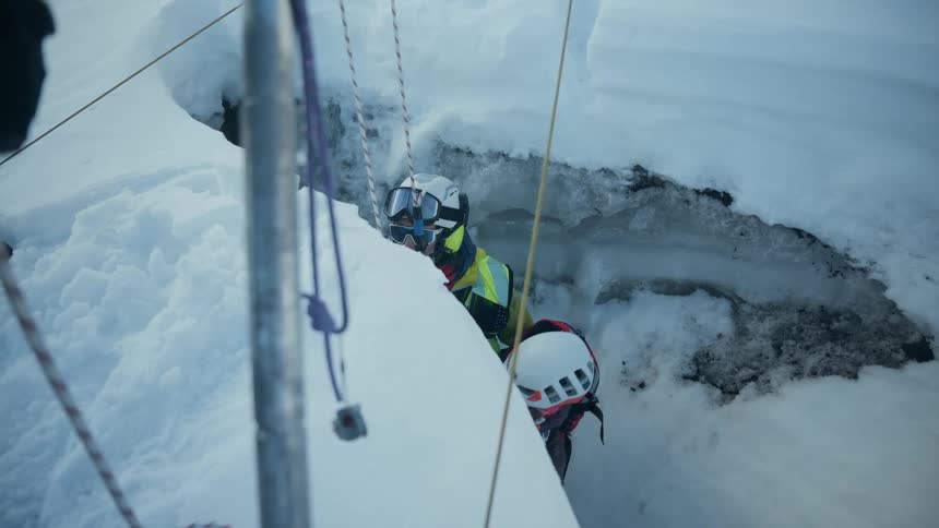 Professional performing a rescue in a glacier crevasse using ropes and helmet