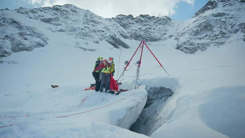 Rescue team positioned on a glacier beside a crevasse with an anchoring system set up