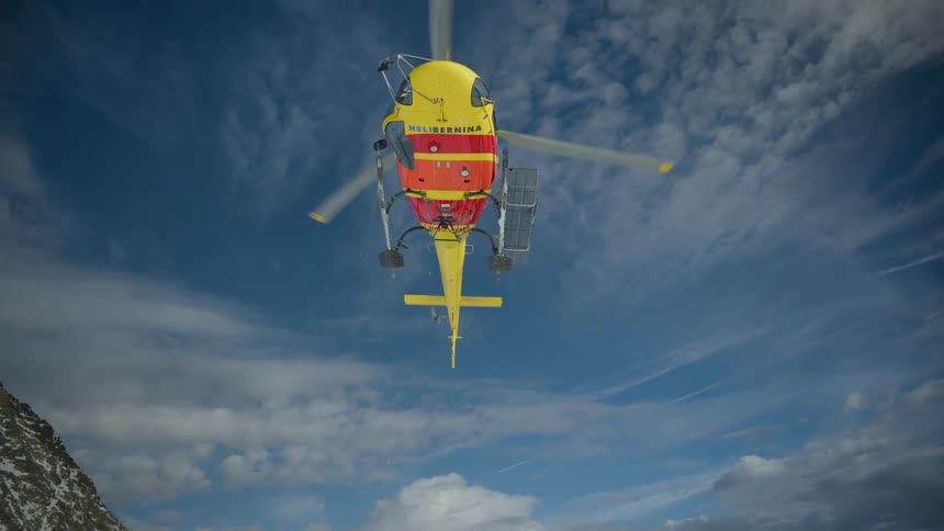 A rescue worker shuts a helicopter door as it lifts off a snowcovered mountain