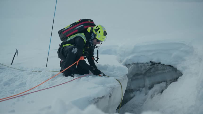 Man at the edge of a snow covered mountain cliff holding a rope
