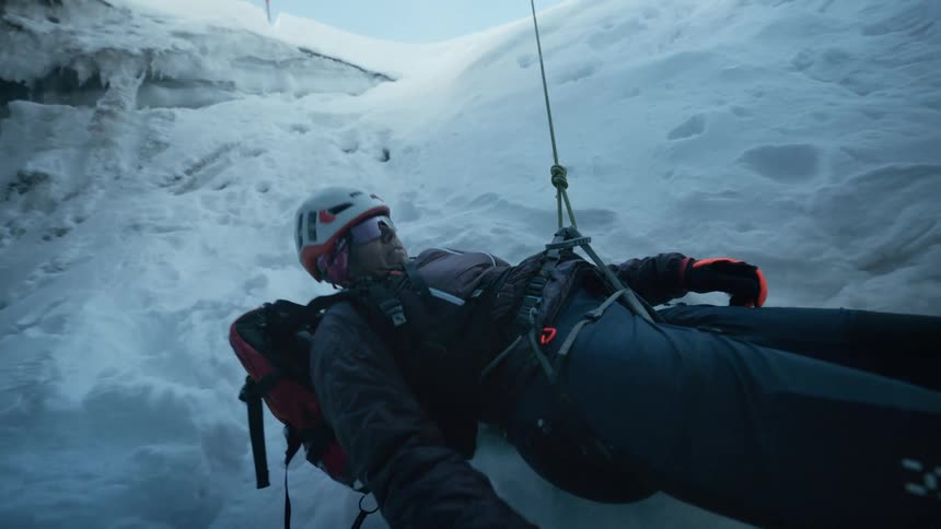 A man hanging from a harness in a snowy mountain