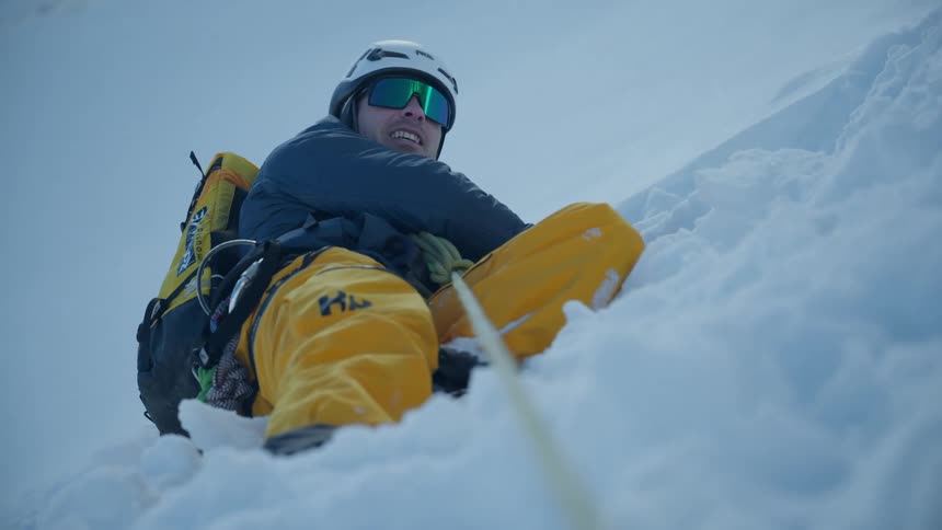 Mountaineer wearing helmet and goggles climbing a snowcovered slope secured by a rope