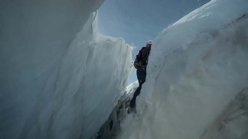 A climber wearing a helmet and safety gear attempts to leap across a wide gap in a snowy glacier they lose their footing during the jump and fall deep into the crevasse while secured by a safety rope