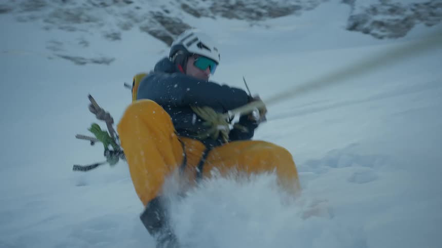Mountaineer slipping on a snowy slope while holding a safety rope