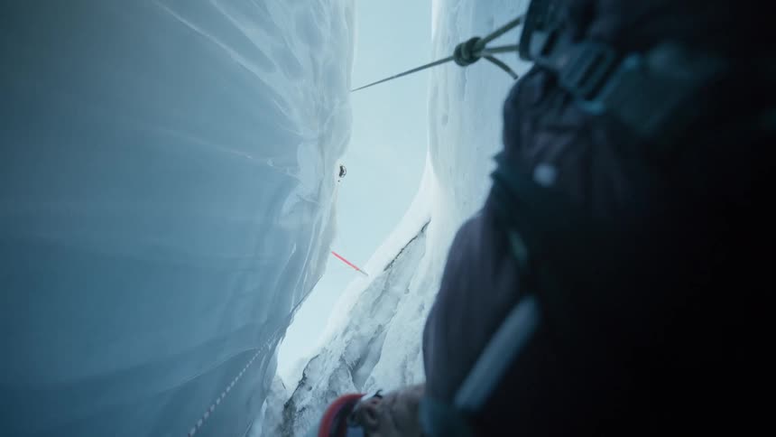 Vertical view of a glacier crevasse with a mountaineer secured by a rope between ice walls