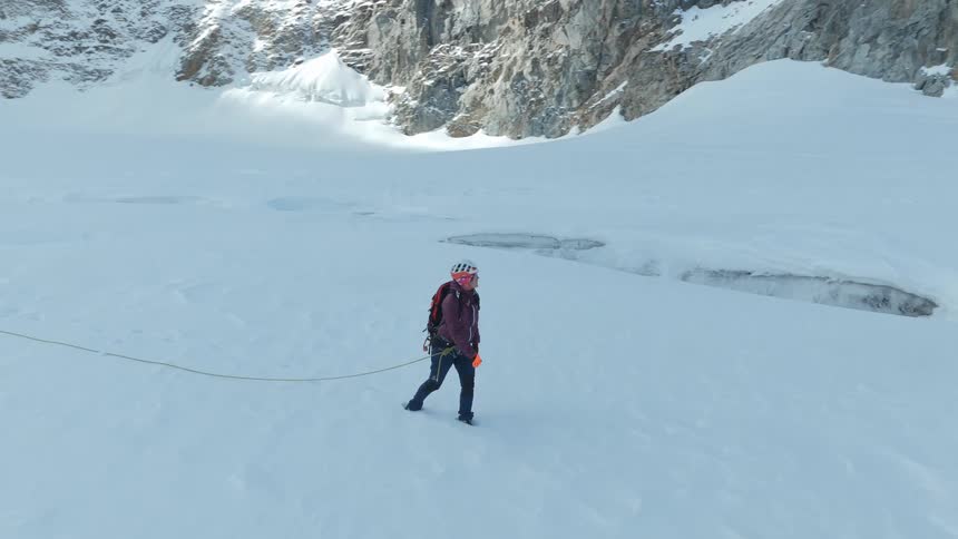 Three people walking in a straight line up a snowcovered mountain in winter at midday tied together with a rope as they move across the snow