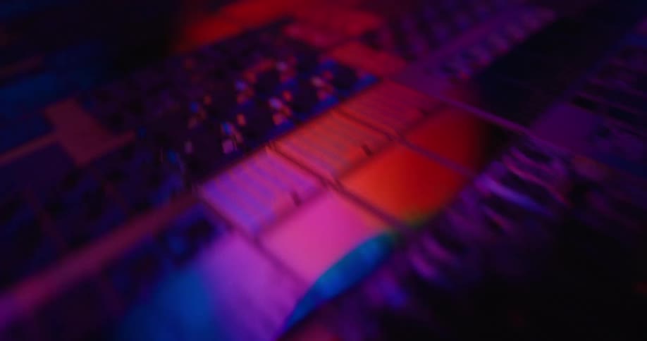 A close view shows rows of square computer microchips with intricate circuits glowing under shifting red and green and blue lights in a dark technical setting