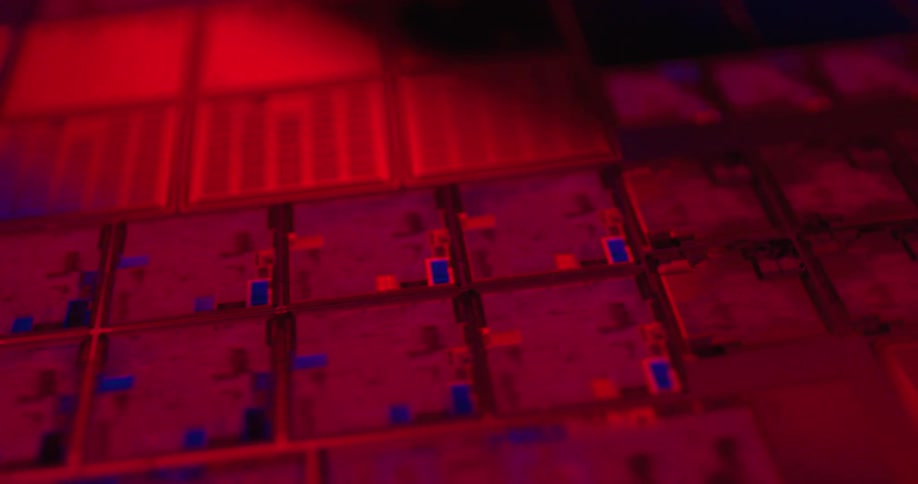 A close view shows rows of square computer microchips with intricate circuits glowing under shifting blue and red and purple lights in a dark technical setting