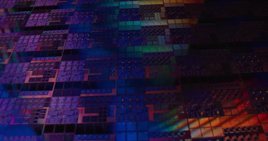 A close view shows rows of square computer microchips with intricate circuits glowing under shifting blue and purple and green lights in a dark technical setting