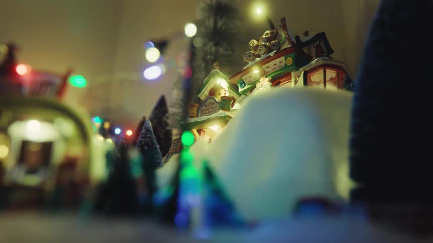 Miniature santa and his sleigh move through the air over christmas decor containing buildings and miniature conifers