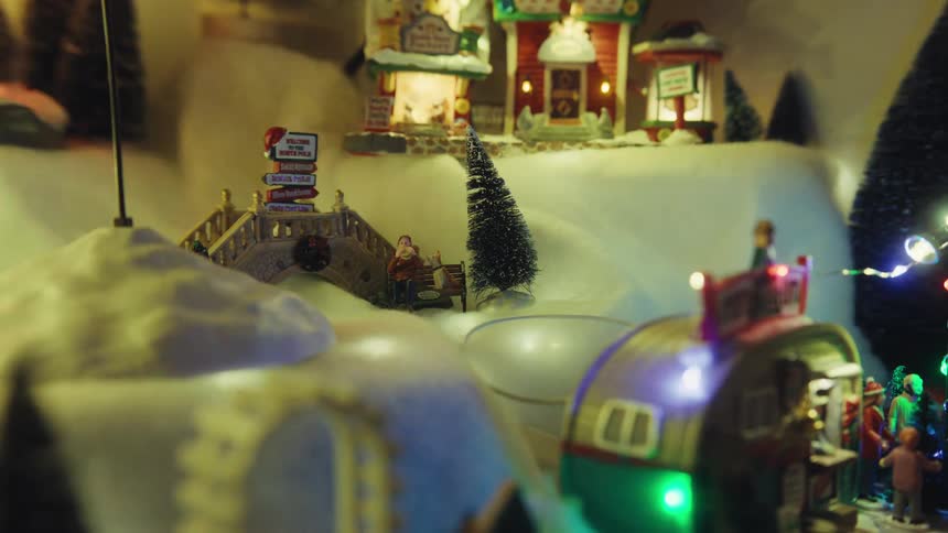 Christmas lights shine onto christmas decorations including figurines and small trees
