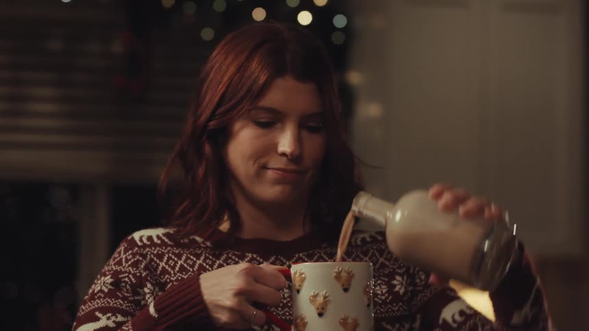 Woman pours a drink into a mug decorated with reindeer figures indoors