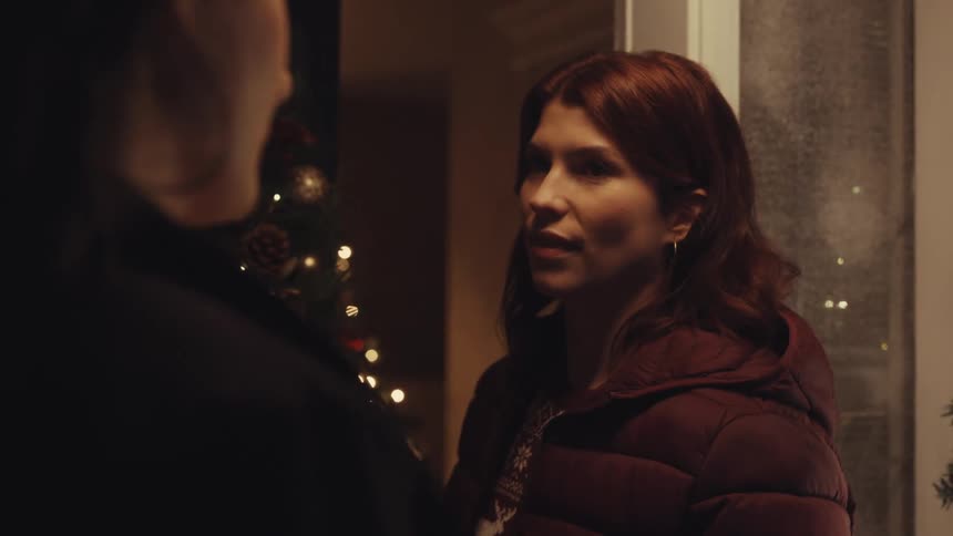 Two people stand near a christmas wreath before entering a home