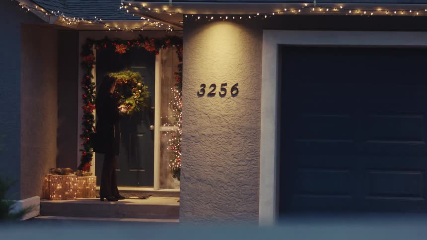 Woman completes a phone call after arriving at a house decorated for christmas before another woman arrives to surprise her