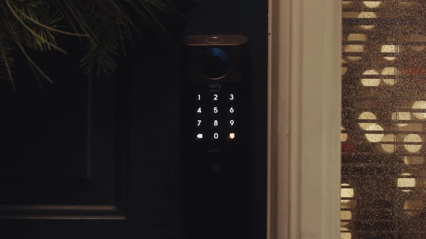 A close view of a person using a finger to press numbers on a glowing smart lock keypad attached to a dark door at night before the door opens to a warm interior