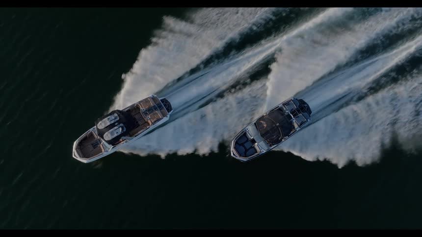 The video features an overhead aerial shot of two motorboats cruising sidebyside at high speed across dark waterboth vessels leave behind long powerful white wakes as they navigate the calm surface in a parallel formation