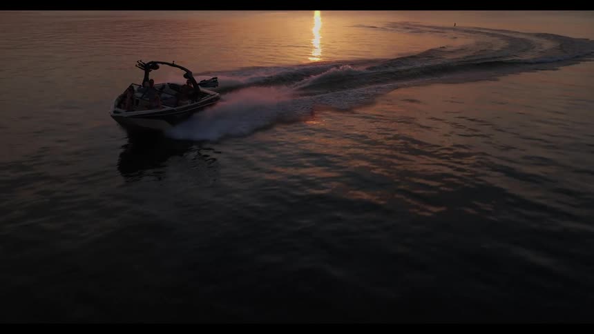 Speedboat moves across the sea at sunset leaving a trail of foam on the water