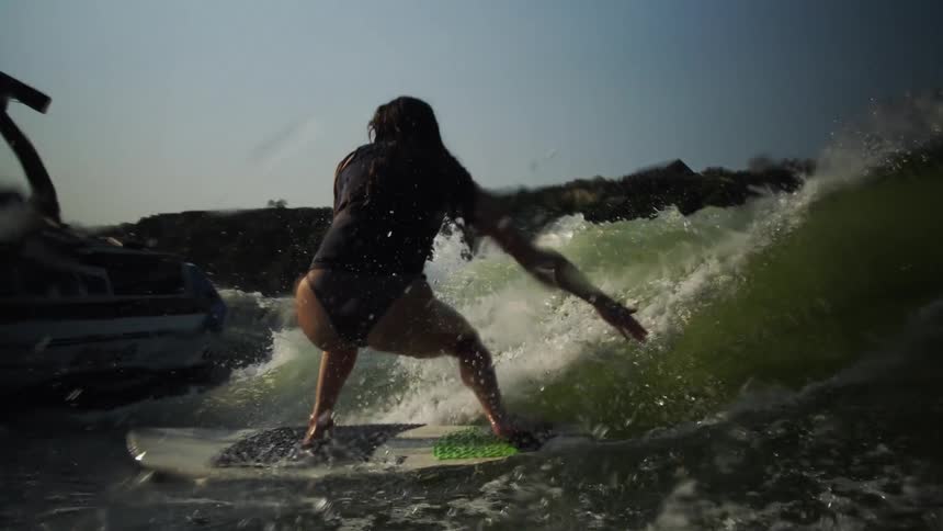 Person surfs on a wave created by a boat on a lake under a clear sky