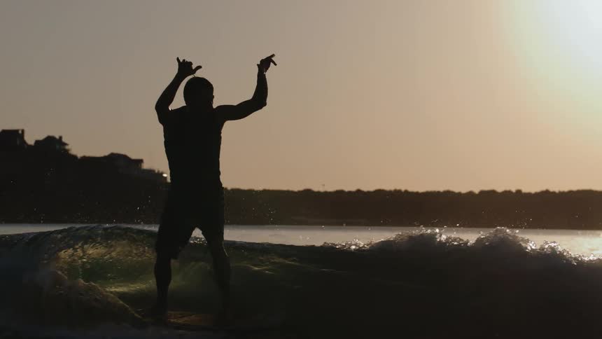 Male surfer silhouetted by the sun shining from the red tinted sky balances on a surfboard