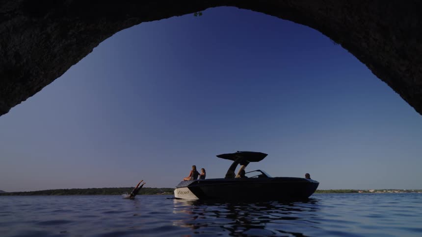 A person dives off a boat into water beneath a cave
