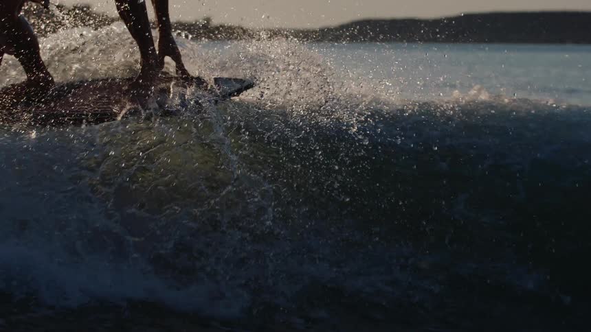 A person wakeboards across a sunlit wave kicking up a spray of water against a backdrop of distant hills the lowangle lighting captures the athletes silhouette as they maintain balance on the board during the golden hour